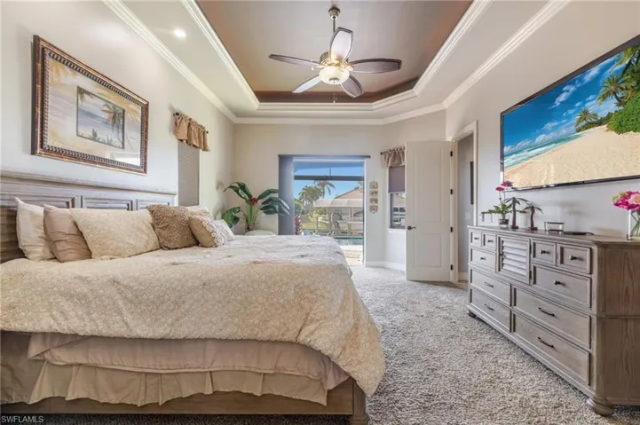Bedroom featuring a raised ceiling, carpet, ceiling fan, and ornamental molding