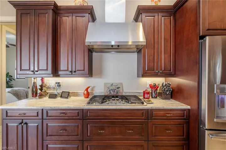 Kitchen with wall chimney exhaust hood, appliances with stainless steel finishes, and light stone counters