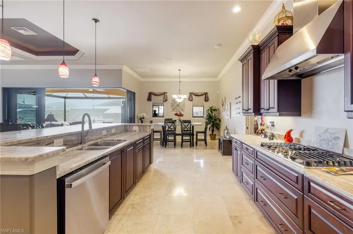 Kitchen featuring pendant lighting, crown molding, stainless steel appliances, wall chimney range hood, and light stone counters