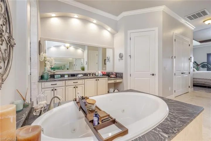 Ensuite bathroom featuring a whirlpool tub, ornamental molding, and vanity