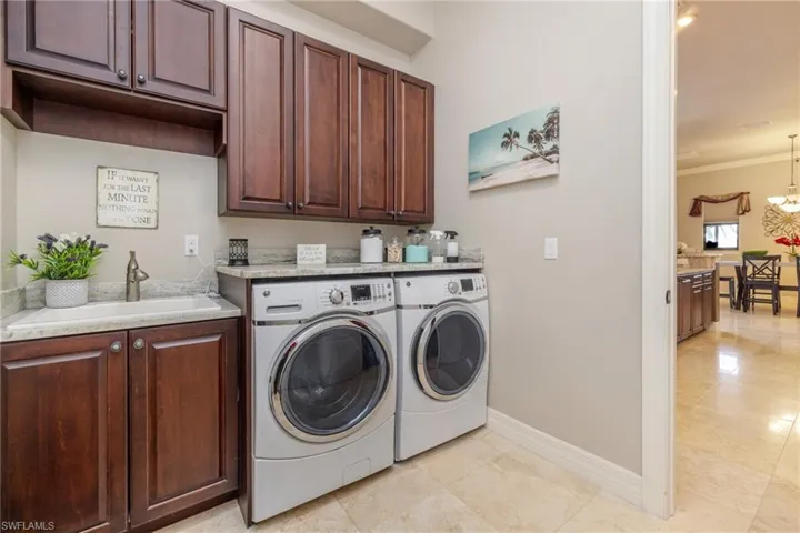 Washroom featuring cabinet space, washing machine and dryer, a chandelier, light tile patterned flooring, and crown molding