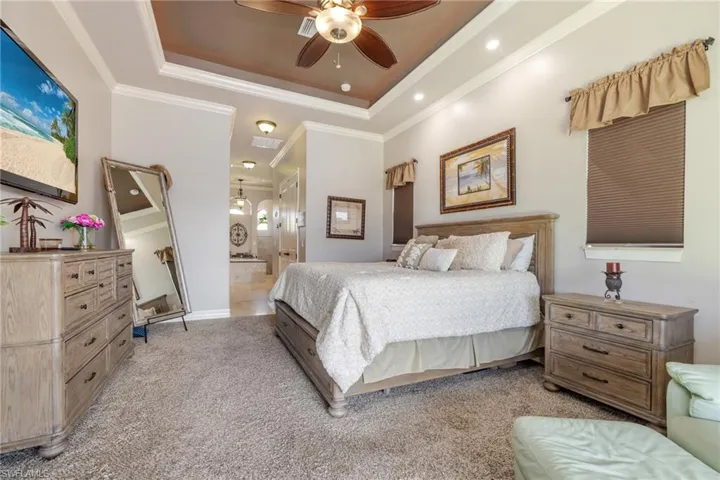 Bedroom with a raised ceiling, ornamental molding, ceiling fan, light carpet, and recessed lighting