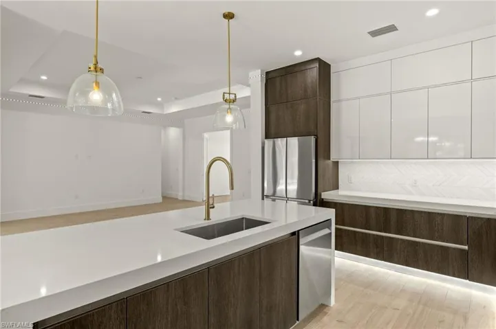 Kitchen with white cabinets, a sink, dark brown cabinetry, a tray ceiling, and stainless steel appliances