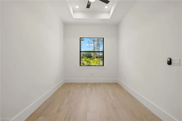 Empty room with light wood-style flooring, baseboards, a raised ceiling, and a ceiling fan
