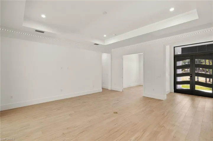 Empty room with light wood-style floors, recessed lighting, a raised ceiling, french doors, and baseboards