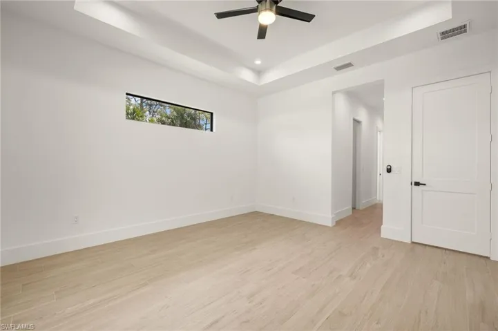 Spare room with light wood-style floors, visible vents, a tray ceiling, and a ceiling fan