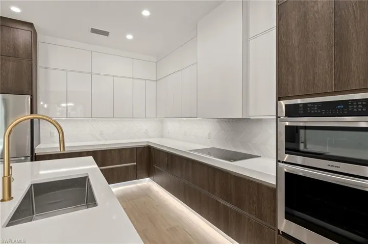 Kitchen featuring white cabinets, modern cabinets, a sink, dark brown cabinets, and double oven