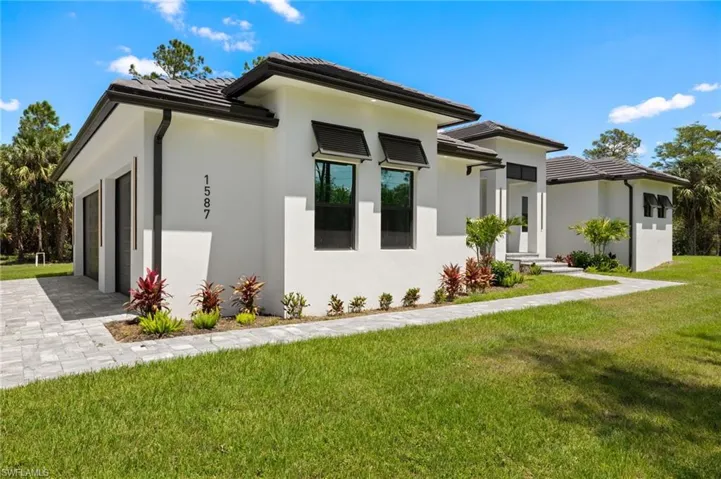 View of side of home featuring a yard, a garage, a tile roof, stucco siding, and driveway
