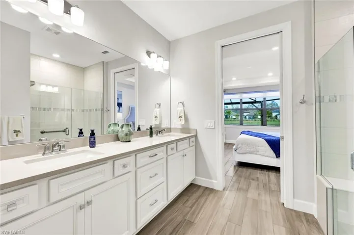 Bathroom featuring a stall shower, double vanity, connected bathroom, and wood finish floors