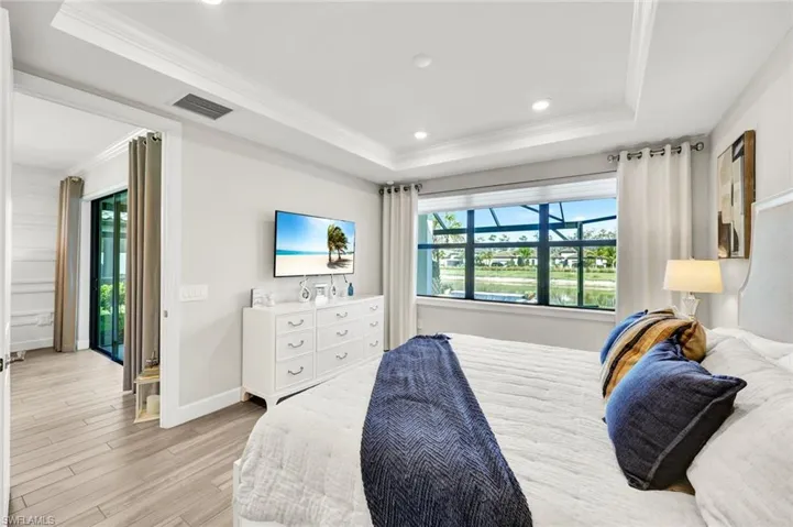Bedroom featuring ornamental molding, light wood finished floors, recessed lighting, and a raised ceiling
