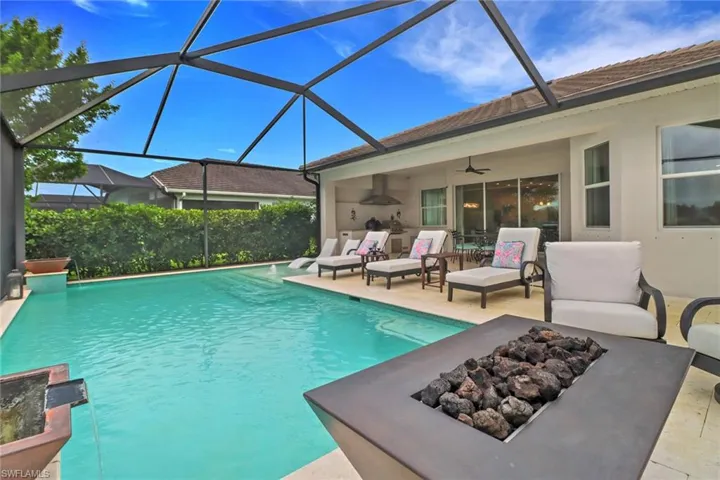 View of pool featuring a patio, ceiling fan, glass enclosure, and an outdoor fire pit