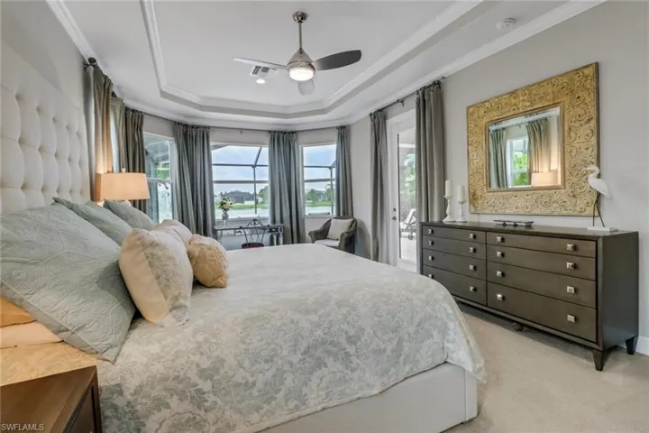 Bedroom featuring ceiling fan, multiple windows, light colored carpet, and a tray ceiling