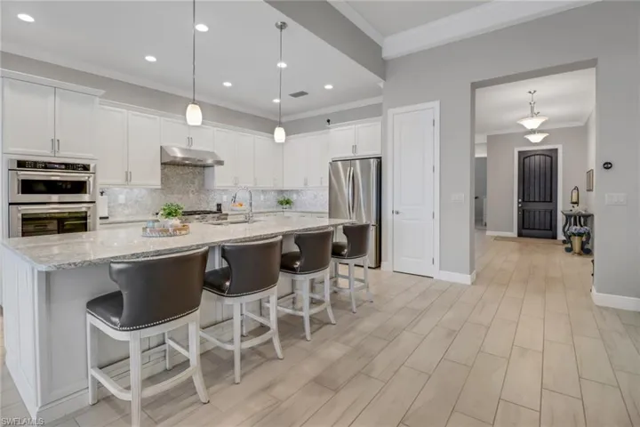 Kitchen featuring stainless steel appliances, pendant lighting, white cabinets, quartz countertops, and backsplash