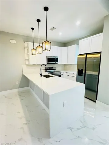 Kitchen with a peninsula, visible vents, stainless steel appliances, marble finish floor, and a sink