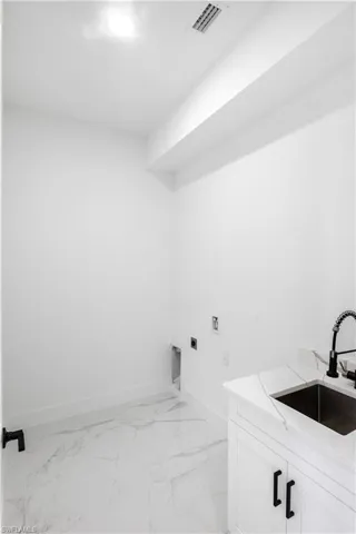 Laundry area with electric dryer hookup, cabinet space, hookup for a washing machine, and light marble finish floors