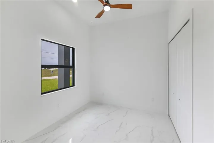 Unfurnished bedroom featuring a ceiling fan, light marble finish floors, and a closet