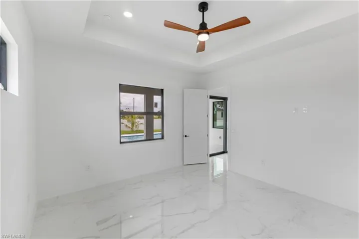 Empty room featuring a ceiling fan, light marble finish flooring, recessed lighting, and a tray ceiling