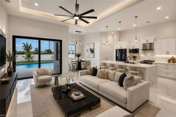 Open-concept living area with tray ceiling, recessed lighting, large format tile flooring, and sliding glass doors to a swimming pool