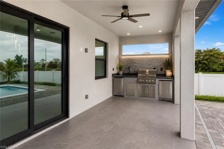 Covered outdoor patio featuring an integrated kitchen with stainless steel appliances, stone tile backsplash, and a ceiling fan