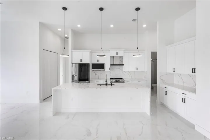 Kitchen with light stone countertops, white cabinetry, a high ceiling, stainless steel appliances, and decorative backsplash