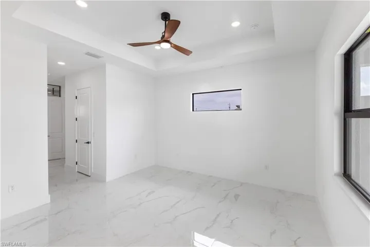 Spare room with healthy amount of natural light, ceiling fan, recessed lighting, a raised ceiling, and light marble finish floors