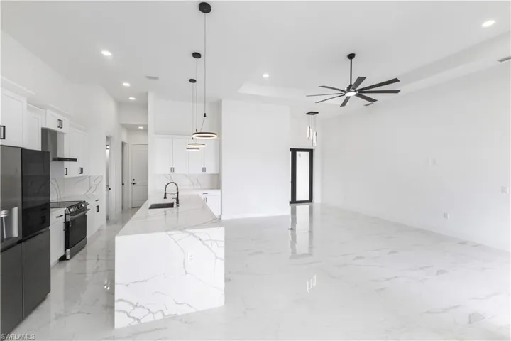 Kitchen featuring white cabinets, stainless steel appliances, light stone countertops, a center island with sink, and decorative light fixtures