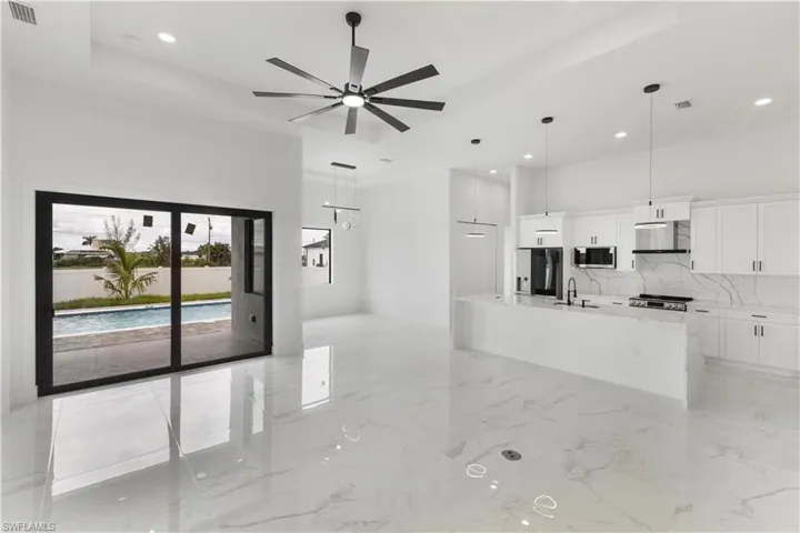 Kitchen with a tray ceiling, white cabinets, light stone countertops, a kitchen island with sink, and stainless steel appliances