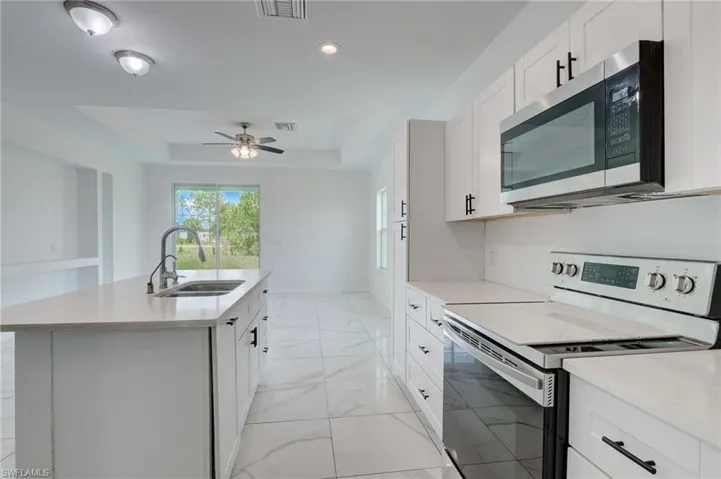 Kitchen with a center island with sink, ceiling fan, a raised ceiling, sink, and electric stove
