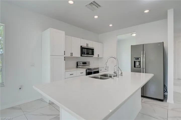 Kitchen with appliances with stainless steel finishes, white cabinetry, sink, and light tile floors