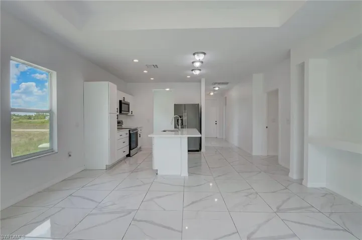Kitchen with appliances with stainless steel finishes, white cabinets, an island with sink, and light tile floors