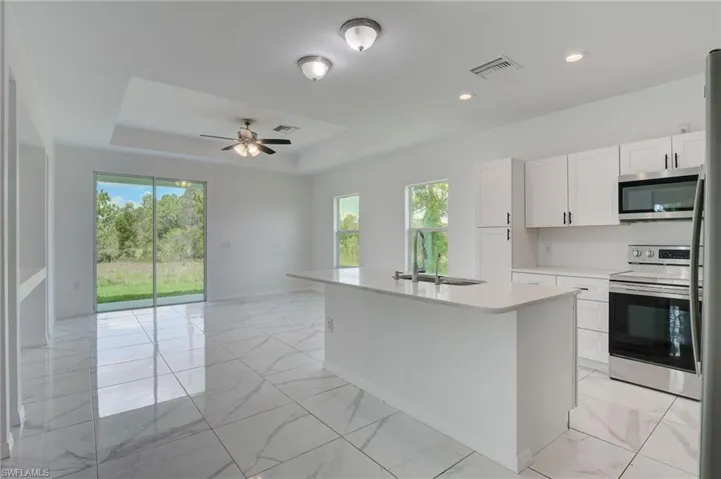 Kitchen featuring ceiling fan, a raised ceiling, light tile floors, sink, and range with electric stovetop