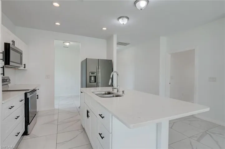 Kitchen with stainless steel appliances, a center island with sink, sink, and light tile floors