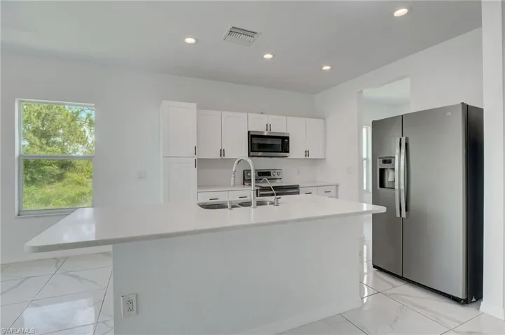 Kitchen featuring stainless steel appliances, sink, an island with sink, and light tile flooring