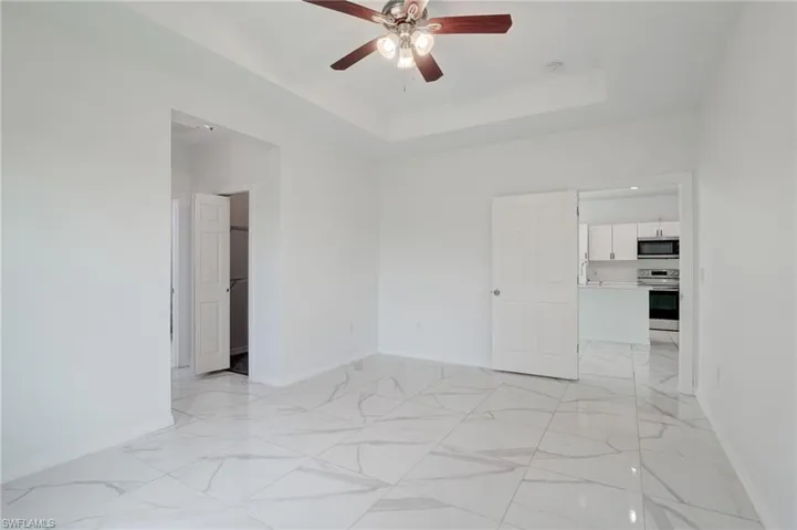 Tiled empty room with ceiling fan and a raised ceiling