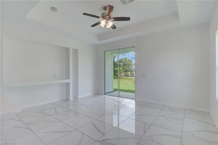 Spare room featuring ceiling fan, a tray ceiling, and light tile floors
