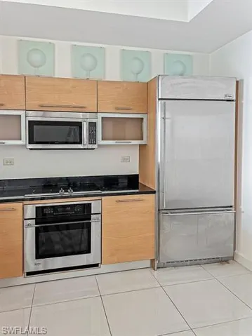 Kitchen featuring built in appliances, light tile patterned floors, dark stone countertops, light brown cabinetry, and modern cabinets