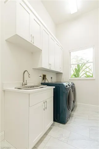Laundry area with cabinet space, washer and clothes dryer, and light marble finish flooring