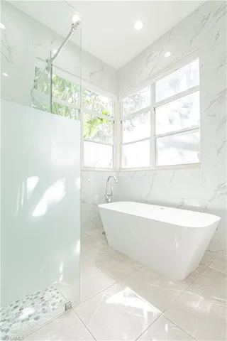 Bathroom with healthy amount of natural light, a freestanding bath, a walk in shower, tile walls, and stone wall