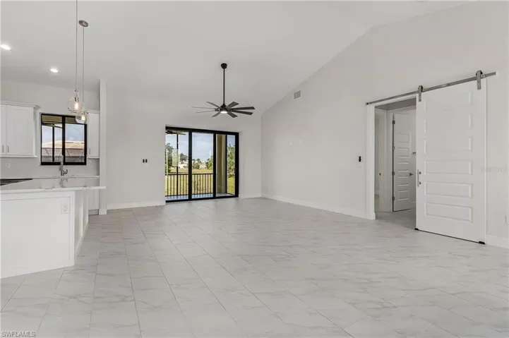 Unfurnished living room featuring light tile patterned flooring, high vaulted ceiling, ceiling fan, and a barn door