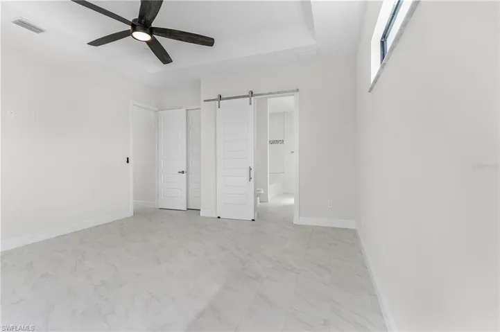 Unfurnished bedroom featuring light tile patterned flooring, a barn door, and ceiling fan