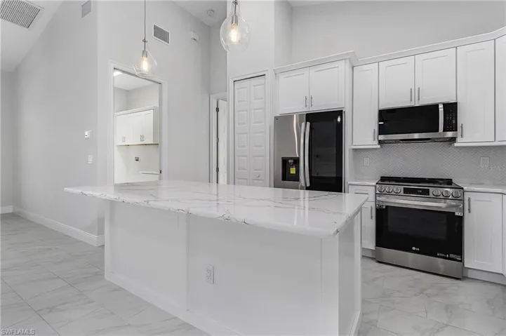 Kitchen with white cabinetry, appliances with stainless steel finishes, pendant lighting, and light tile patterned floors