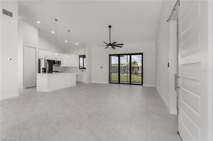 Unfurnished living room featuring high vaulted ceiling, ceiling fan, a barn door, and light tile patterned floors