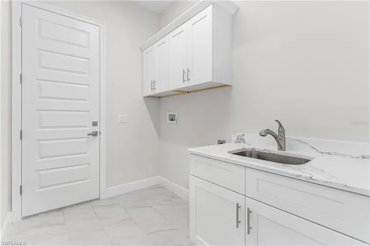 Clothes washing area featuring sink, cabinets, light tile patterned floors, and washer hookup