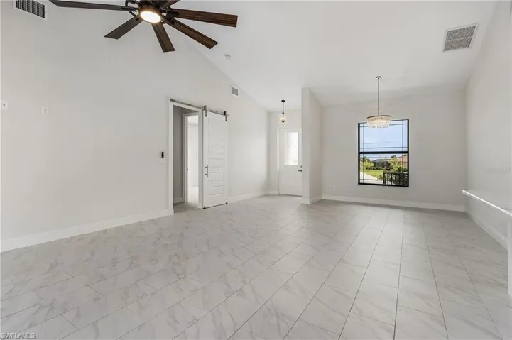 Tiled empty room with ceiling fan with notable chandelier, a barn door, and high vaulted ceiling
