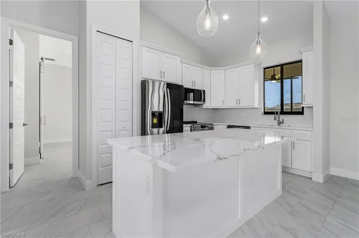 Kitchen with light tile patterned flooring, vaulted ceiling, a center island, appliances with stainless steel finishes, and decorative light fixtures