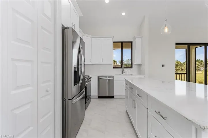 Kitchen with white cabinetry, stainless steel appliances, pendant lighting, light stone counters, and light tile patterned floors