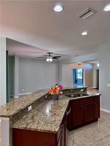 Kitchen featuring stainless steel dishwasher, ceiling fan, sink, stone counters, and light tile patterned flooring