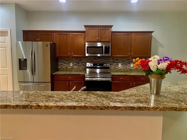 Kitchen with tasteful backsplash, light stone counters, and appliances with stainless steel finishes