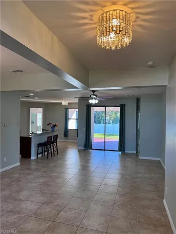 Spare room featuring tile patterned flooring, ceiling fan with notable chandelier, and a healthy amount of sunlight