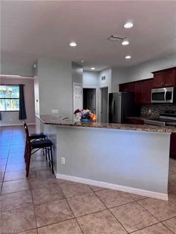 Kitchen featuring stone counters, stainless steel appliances, an inviting chandelier, decorative backsplash, and light tile patterned floors